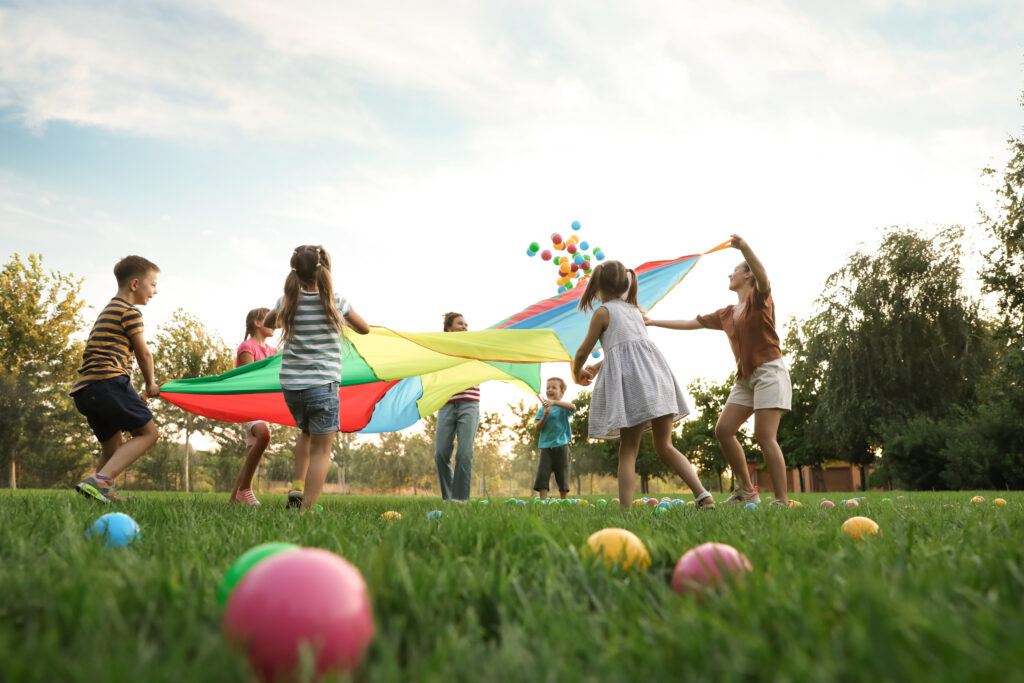 Group of children and teachers playing with rainbow playground p AdobeStock 455469145 1024x683